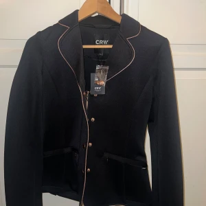 Svart jacka från CRW - Snygg svart kavaj från CRW med guldknappar och dragkedja. Kavajen har en elegant design med kontrasterande kantdetaljer och är perfekt för en stilren look. 