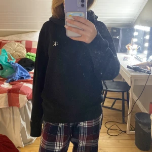 Svart hoodie från Calvin Klein - Säljer en stilren svart hoodie från Calvin Klein med det klassiska CK-logotypen på bröstet. Hoodien har långa ärmar och en bekväm passform, perfekt för en avslappnad look.