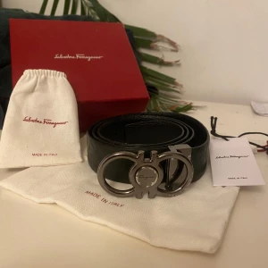 Mörkgrönt bälte från Salvatore Ferragamo - Elegant mörkgrönt skärp från Salvatore Ferragamo med en stilren silverfärgad spänne. Tillverkat i Italien, detta skärp har en subtilt mönstrad yta som ger en exklusiv känsla. Perfekt för att lyfta vilken outfit som helst. Har ett egengjort hål.
