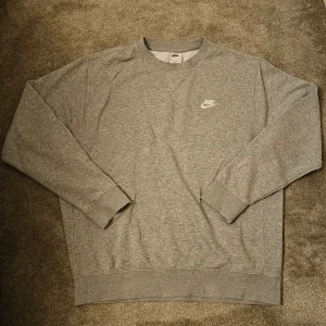 Grå sweatshirt från Nike - Säljer en klassisk grå sweatshirt från Nike med rund hals och långärmad design. Tröjan har en broderad Nike-logga på bröstet och är tillverkad i ett mjukt material för extra komfort.
