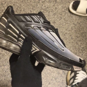Nike Air Max Plus Tuned - Snygga Nike Air Max Plus Tuned sneakers i svart och grått med en futuristisk design. Skorna har synliga Air Max-dämpningar och en unik snörning. Perfekta för en sportig look.