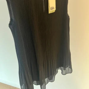 Svart ärmlös topp från H&M - Snygg svart ärmlös topp från H&M med plisserad design. Perfekt för en stilren look. Toppen är i ett lätt och luftigt material. Prislappen är kvar och varan är aldrig använd 