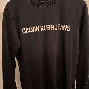 Svart tröja från Calvin Klein Jeans - Snygg svart tröja från Calvin Klein Jeans med deras logga tryckt på framsidan. Tröjan har långa ärmar och en rund halsringning. Perfekt för en stilren och avslappnad look.