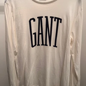 Vit långärmad tröja från GANT - Säljer en stilren vit långärmad tröja från GANT med svart logotyp på framsidan. Perfekt för en avslappnad och trendig look.