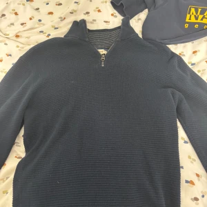 Mörkblå tröja med dragkedja - Säljer en stilren mörkblå tröja med dragkedja. Perfekt för kyliga dagar med sin bekväma passform och ribbade detaljer. Passar både till vardags och mer avslappnade tillfällen.