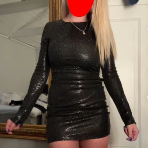 Svart glittrig klänning nyårsklänning - Snygg svart glittrig klänning med lång ärm och tight passform. Perfekt för nyår. Klänningen är kort och har en elegant look.