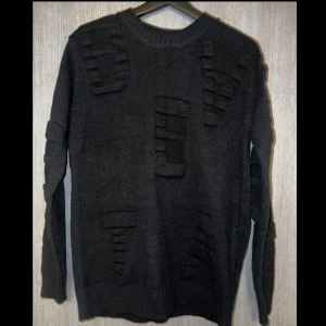 Svart stickad tröja med texturdetaljer - Snygg svart stickad tröja med unika texturdetaljer som ger en cool look. Tröjan har långa ärmar och ribbade muddar vid ärmslut och nederkant.