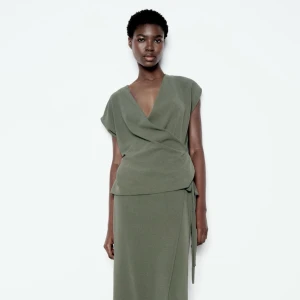 Olivgrön omlottopp från Zara - Snygg olivgrön omlottopp från Zara med korta ärmar och v-ringning. Perfekt för en stilren look. prislappen kvar, aldrig använd 