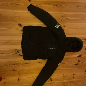 Sail Racing dunjacka - Mycket skön, varm och snygg svart dunjacka från Sail Racing med huva och dragkedja. Jackan har logotypdetaljer på bröstet och ärmarna, vilket ger en sportig look. Perfekt nu när det börjar bli kallare! Jackan är i toppskick. Nypris ligger på 4200kr. Jackan är i storlek M men passar S också 