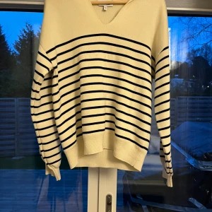 Randig tröja från & Other Stories - Säljer en stilren randig tröja från & Other Stories i beige och svart. Tröjan har en v-ringad hals och långa ärmar. Den är tillverkad i ett mjukt material som ger en skön passform.