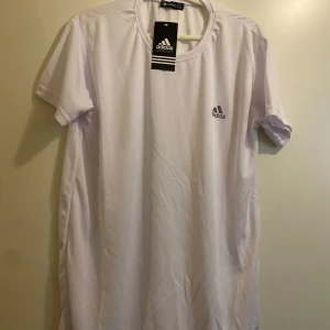 Vit t-shirt från Adidas - Snygg vit t-shirt från Adidas med korta ärmar och klassisk rund hals. Perfekt för träning eller en avslappnad stil. Adidas-loggan är tryckt på bröstet.