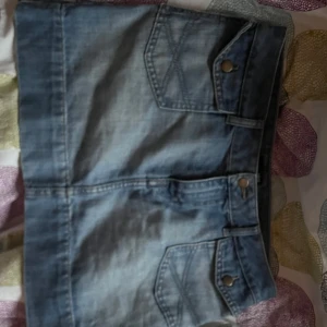 Blå jeanskjol från H&M - Snygg blå jeanskjol från H&M med fickor fram och bak. Kjolen har en klassisk design med knappar och bälteshällor. Perfekt för en avslappnad stil.