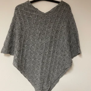 Grå stickad poncho från KappAhl - Säljer en stilren grå stickad poncho från KappAhl. Den har ett vackert hålmönster och en bekväm passform som passar perfekt för kyliga dagar. Perfekt att slänga över en tröja för extra värme. (Finns dock ingen storleks lapp kvar på den, men då jag är en M vanligtvis skulle jag säga att den passar mig utmärkt. Därav Storlek M)