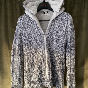 Fodrad Cardigan Jacka  - Tja! Säljer en grå stickad cardigan jacka med dragkedja och mysigt fleecefoder. Tröjan har ett snyggt mönster och långa ärmar, perfekt för kyliga dagar. Huvan ger extra värme och stil och går även att ta av om man vill det. Aningen liten i storleken. Vid minsta fråga eller fundering hör av er🤝