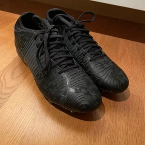 Svarta fotbollsskor från Puma - Säljer ett par svarta fotbollsskor från Puma med snörning. Skorna har en stilren design med mönstrad yta och dobbar för bra grepp på planen. Perfekta för fotbollsträning och matcher. Helt Nya, aldrig använda. Köpta för 1599