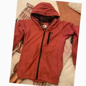 Röd vindjacka med huva - Snygg rosa vindjacka från Five Seasons med huva och dragkedja. Jackan har en praktisk bröstficka med dragkedja och elastiska muddar vid ärmslut. Perfekt för blåsiga dagar.