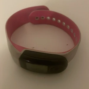 Vit och rosa sportklocka från Nike - Säljer en sport puls klocka från Nike med vit utsida och rosa insida. Batteri måste bytas.Klockan har en digital display och ett justerbart armband med flera hål för perfekt passform. Perfekt för träning och vardagsbruk.