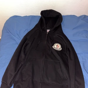 Svart Moncler hoodie - Säljer en svart hoodie från Moncler då den är för liten för mig som är 176 cm lång. Tröjan är stilren och har en insida som är filt liknande och varm. Tröjan är i storlek S. Använd endast en gång.  Lappen som satt i hoodien när den köptes sitter kvar. Man får även med påsen som hoodien kom i. Bättre pris vid snabb affär!