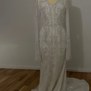 Vit långklänning med stenar - Elegant vit långklänning med glittrande paljetter och intrikata mönster. Klänningen har långa ärmar och en v-ringad hals. Perfekt för speciella tillfällen med sin lyxiga design och detaljerade broderier. Funkar perfekt för nikkah går att ha vita/beiga ärmar under ärmarna utan att de ser konstigt ut. Klänningen har inga defekter eller är smutsig någonstans. Endast använd inomhus 1 timme. Går att testa klänningen i Göteborg.