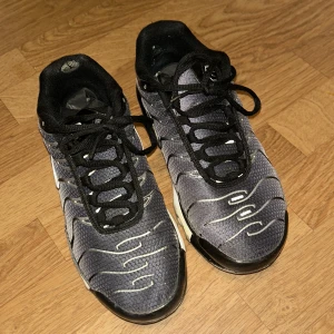 Nike TNS - Snygga Nike sneakers i grått och svart med vågformade detaljer och svart snörning. Perfekta för en sportig look.