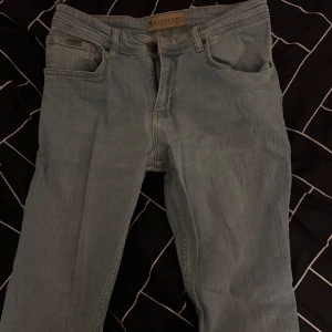 Ljusblå jeans från Burberry - Snygga ljusblå jeans från Burberry med klassisk femficksdesign och knappgylf. De har en läderpatch med Burberry-logga på baksidan och subtila detaljer vid fickorna. Perfekta för en stilren look. Använda 1 gång och inget mer än så, inga skador eller så finns på jeansen priset kan säkert justeras och byten kan tas emot. 