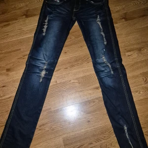Mörkblå jeans med slitningar från Diesel med stretch I tyg, waist 29 - Snygga mörkblå jeans med slitningar på framsidan för en trendig look. De har en klassisk femficksdesign och kontrasterande sömmar. Perfekta för en avslappnad stil.. stretch I tyg för perfekt passform, sitter som ett smäck! Som nya length 32