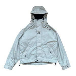 Helly Hansen jacka regnjacka vindjacka boxy baggy oversized retro y2k vintage  - Säljer en vattenavvisande jacka från Helly Hansen med justerbar huva och dragkedja. Jackan har elastiska ärmslut och dragsko i nederkant för optimal passform. Perfekt för blåsiga dagar. Small på lappen sitter mer som en medium, pit or pit ca 60cm längd ca 65cm