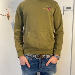 Olivgrön GANT hoodie - GANT | Snygg olivgrön hoodie med ett coolt emblem på bröstet | skick 9/10 | Pris går att diskutera vid snabb affär!