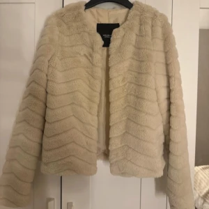 Beige pälsjacka från Vero Moda - Säljer en snygg beige pälsjacka från Vero Moda. Jackan har en mjuk och fluffig textur med långa ärmar. Perfekt för att hålla sig varm och stilren. Använd en gång! 🥰