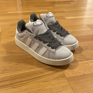 Gråa Adidas campus 00s  - Säljer ett år gråa adidas campus 00 då dom inte riktigt är min stil, fick dom i födelsedags present och de är aldrig använda.