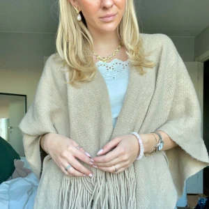 Beige stickad poncho med fransar - Poncho med trekvartsärmar🤎