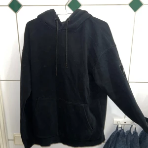 Svart hoodie från Jack & Jones - Säljer en svart hoodie från Jack & Jones med en klassisk design. Den har en stor ficka framtill och justerbar huva med dragsko. Perfekt för en avslappnad stil.
