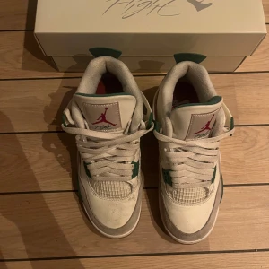 Nike Air Jordans 4 med gröna detaljer - Säljer ett par Nike Air Jordans i vitt med gröna detaljer. Skorna har snörning och en klassisk design med Nike SB-logga på hälen. Perfekta för sneaker-entusiaster!