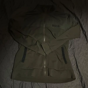 Grön zip tröja från Hugo Boss - Snygg grön zip tröja från Hugo Boss med broderad logga på bröstet. Perfekt för en stilren look.