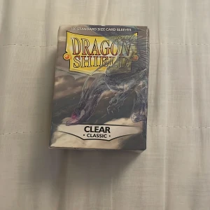 Dragon Shield kortfodral/ kpop photocards - Säljer en förpackning med ~80 standardstorlek kortfodral från Dragon Shield. Dessa är av typen Clear Classic, perfekta för att skydda dina kort med stil. Förpackningen har ett drakmotiv och en berättelse om 'Spook the Wraith Walker' på baksidan. Perfekt för Kpop photocards eller Pokémon tror jag. Jag har använt ungefär 20 st så det är ungefär 80 stycken i förpackningen. 