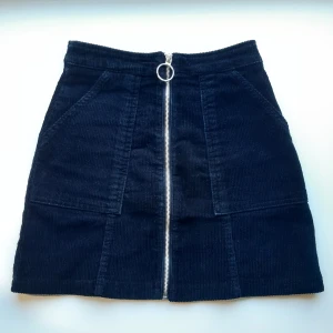 Manchesterkjol - Svart manchesterkjol med fickor och en silvrig dragkedja på framsidan. Den är lite sliten på baksidan från att ha suttits i. Skriv vid frågor. 