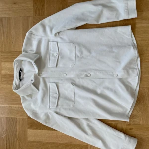 Vit overshirt från Zara - Säljer en stilren vit overshirt från Zara. Perfekt för lager-på-lager under hösten eller våren. Materialet känns robust och är av hög kvalitet.