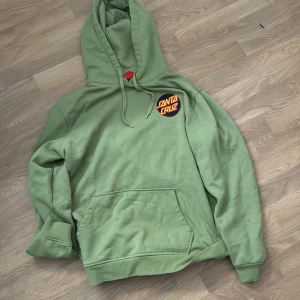 Grön hoodie från Santa Cruz - Säljer en grön hoodie från Santa Cruz i storlek L. Den har en stor logga på ryggen och en mindre på bröstet.Den är i bra skick och superbekväm. Hör av dig om du är intresserad! 💚
