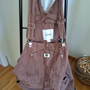 Bruna manchesterbyxor från Monki - Säljer ett par snygga bruna snickarbyxor från Monki. Användes 2 gånger och har en cool hängselstil med justerbara remmar och en praktisk ficka framtill. Perfekta för en avslappnad och trendig look!