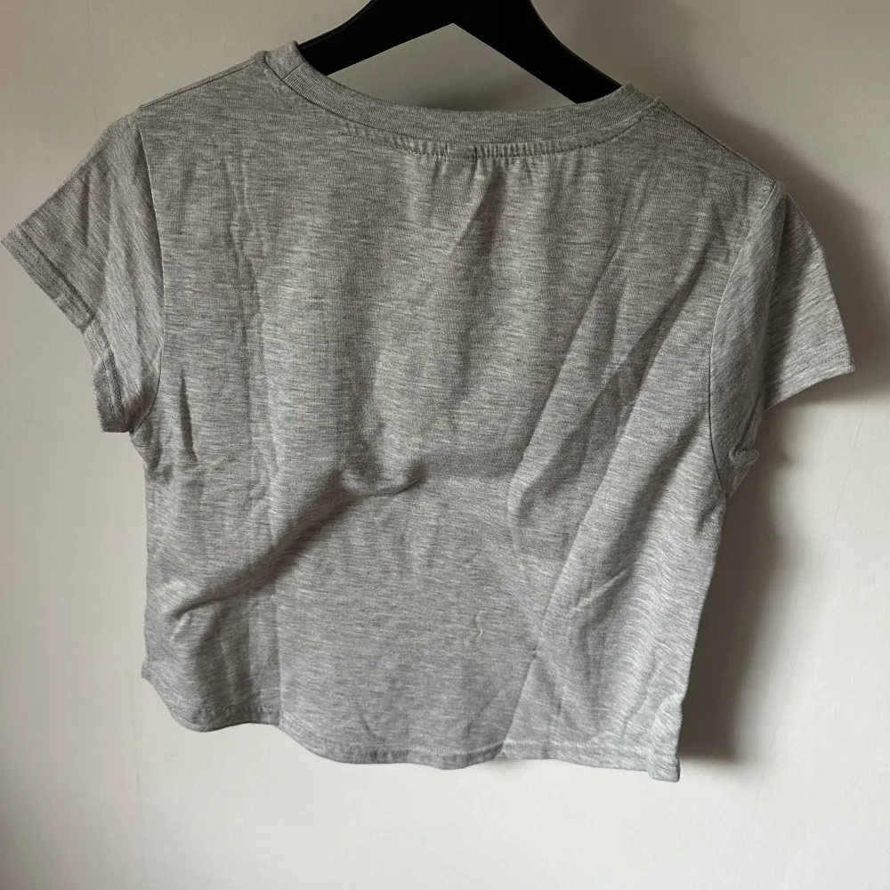 Grå t-shirt som är något kortare i modellen, kan upplevas som en magtröja. Från H&M i storlek S, kan upplevas mer som XS då den är kortare än vanliga t-shirts. Väl använd men inte sliten. . T-shirts.