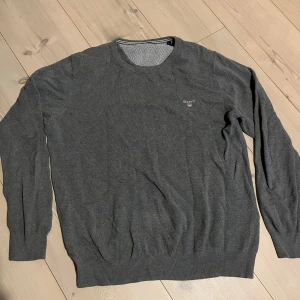 Grå tröja från GANT - Säljer en stilren grå tröja från GANT. Tröjan har en rund halsringning och långa ärmar. Perfekt för en avslappnad och snygg look. Passar bra till både jeans och chinos. Sen har ett litet hål i armhålen men inget man lägger märke till, storöeken är L men kan passa M.