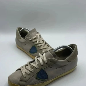 Philipe model - Snygga beige sneakers med blå detaljer på sidan och vita snören. Skorna har en klassisk design med en gummisula i ljusbrun färg. Perfekta för en avslappnad stil.