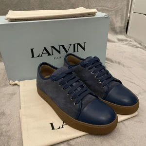 Blå sneakers från Lanvin - Snygga blå sneakers från Lanvin med en kombination av mocka och skinn. Skorna har en brun sula och klassisk snörning. Perfekta för en stilren look.😁 Öppen för frågor och prisförslag🤝