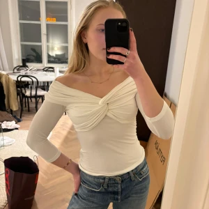 Vit offshoulder topp från Claire Rose x NA-KD - Säljer en stilren vit offshoulder topp från Claire Rose i storlek XS. Toppen har en snygg knutdetalj framtill och trekvartsärmar. Aldrig använd, i storlek XS.