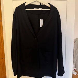 Svart kavaj  Lager157 - Snygg svart kavaj från 157 med enkel knäppning framtill och två fickor. Perfekt för en stilren look. Kavajen har långa ärmar och en klassisk krage.