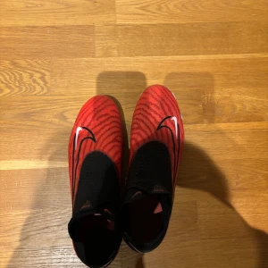 Röda och svarta fotbollsskor från Nike - Tjaaaa! Säljer mina ganska oanvända Nike phantom GX elite. Nytt pris 3149 kr. Konstgräs plan men funkar även på . Box får man även om det behövs(orange Nike box, inte orginal från skorna) Skriv om några frågor