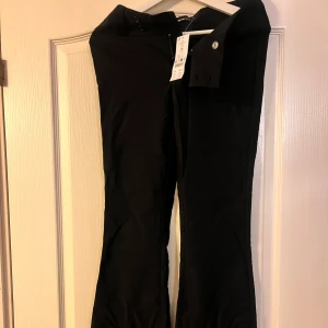 Svarta lågmidjade bootcut kostymbyxor - Snygga svarta lågmidjade bootcut kostymbyxor med dragkedja och knappar. Helt nya med lapp kvar. Storlek 36.