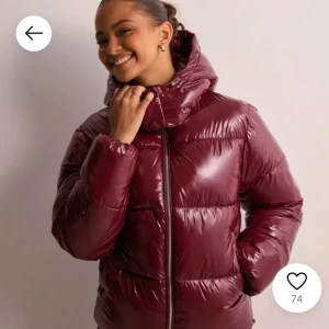 Nelly puffer jacka - Snygg vinröd pufferjacka med glansig finish och dragkedja framtill. Jackan har en praktisk huva och långa ärmar, perfekt för kyliga dagar. Den är både stilren och funktionell.