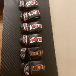  3 Par boxningshandskar - Säljer 3 par svarta boxningshandskar från Fighter. Handskarna har texten 'FIGHTER' i rött och orange på handleden och är designade för träning. De har en justerbar rem för bättre passform och är tillverkade i slitstarkt material.