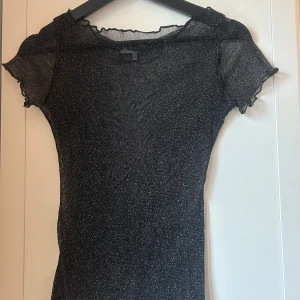 Svart glittrig topp från Chiquelle - Snygg svart glittrig topp från Chiquelle i storlek XS. Toppen har korta ärmar och en fin glittrig yta som ger en festlig känsla. Perfekt för att lysa upp vilken outfit som helst!